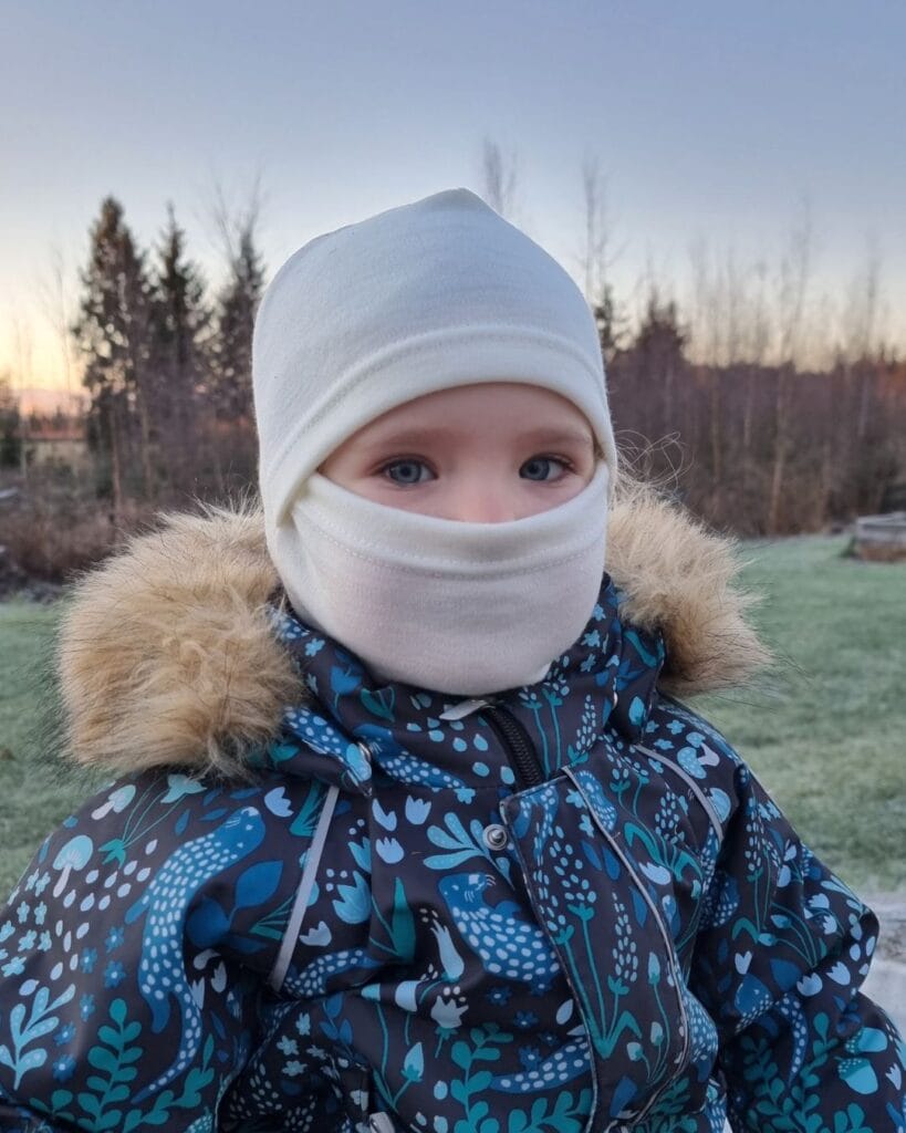 Lasten luonnonvalkoinen merinovilla kypärähuppu (balaclava) pienen lapsen päässä, kasvot suojattuna.
