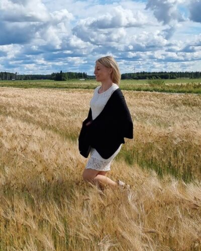Iso musta merinovilla kaulahuivi (hartiahuivi) pitsimekkoisen naisen harteilla, joka kävelee ohrapellolla.