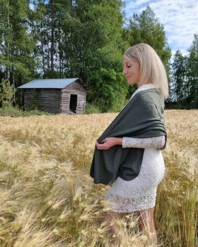Iso metsänvihreä merinovilla kaulahuivi (hartiahuivi) pitsimekkoisen naisen harteilla, joka seisoo ohrapellolla.