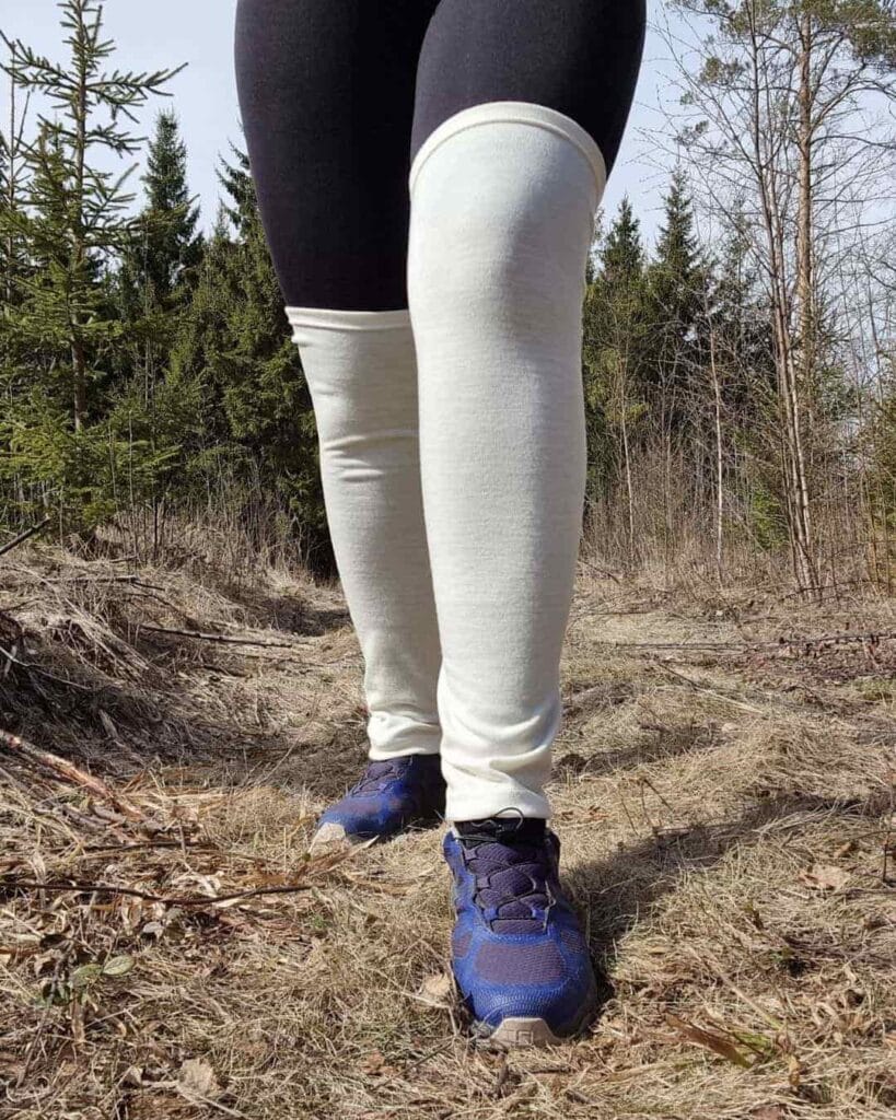Pitkät luonnonvalkoiset merinovilla säärystimet, juoksulenkkareiden kanssa naisen jalassa, polven yli nostettuna.