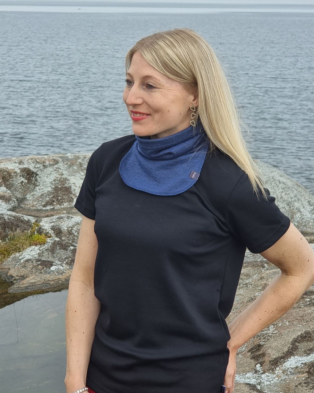 Naisten musta merinovilla t-paita, vaaleahiuksisen siron naisen päällä rantakalliolla.