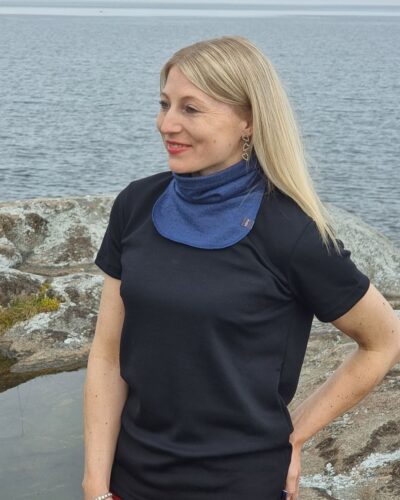 Naisten (farkun) sininen merinovilla tuubikauluri, vaaleahiuksisella naisella. Lähikuva kaulurista naisen kaulassa etuviistosta.