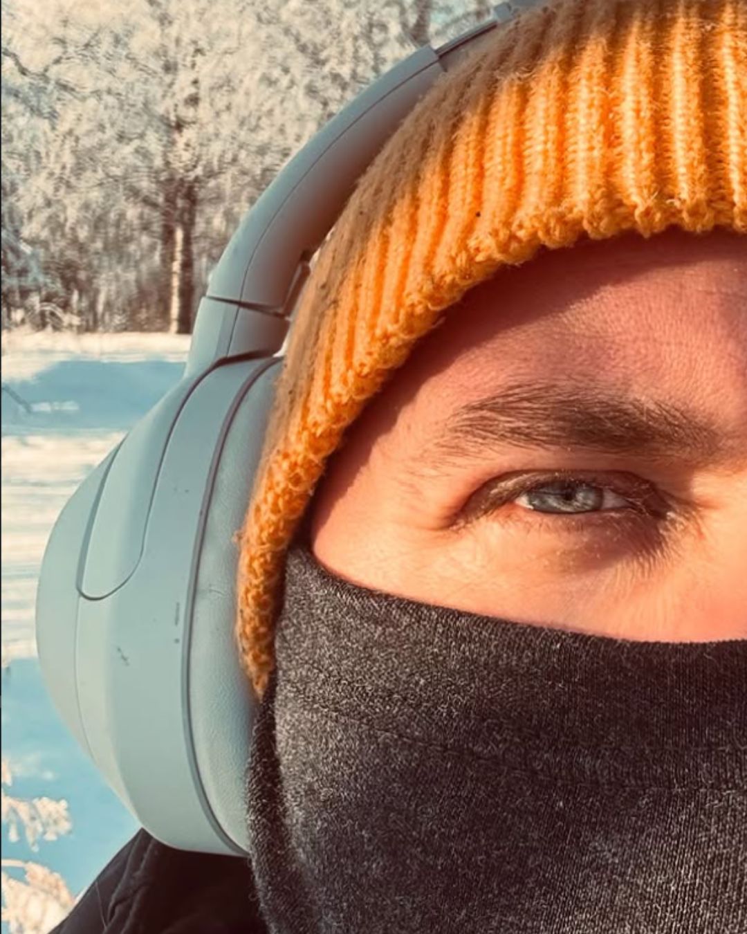 Aikuisten tummanharmaa merinovilla kypärähuppu (balaclava) miehen päässä, pipon alla. Kasvot suojattuna. Lähikuva, jossa näkyy materiaali ja ommel.