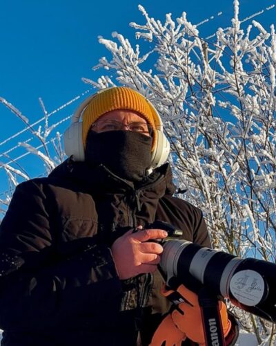 Aikuisten tummanharmaa merinovilla kypärämyssy (balaclava). Aikuisten tummanharmaa merinovilla kypärähuppu (balaclava) miehen päässä, pipon alla. Kasvot suojattuna.