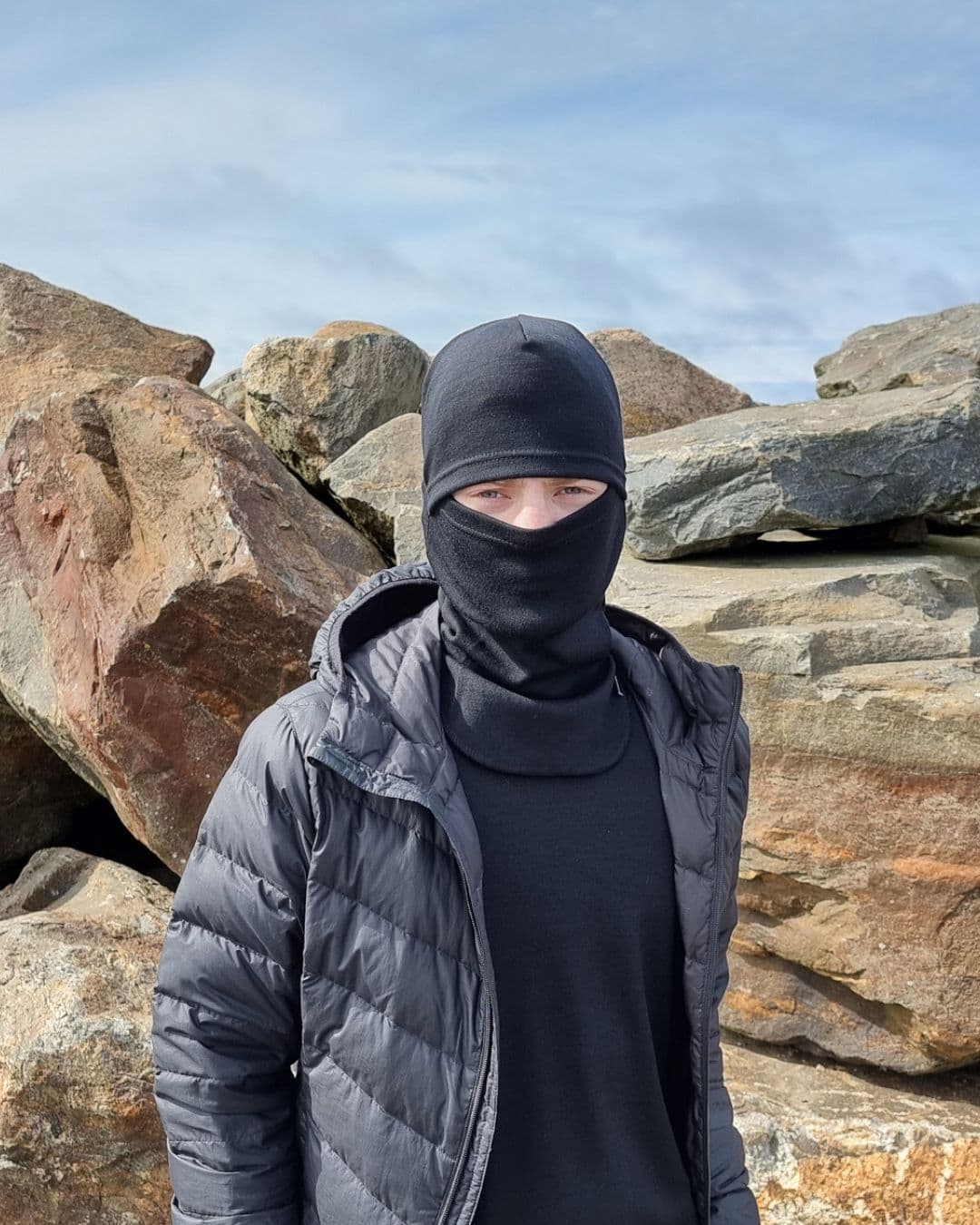Lasten musta merinovilla kypärämyssy (balaclava). Nuoren miehen päässä balaclava kasvojen suojaksi vedettynä.