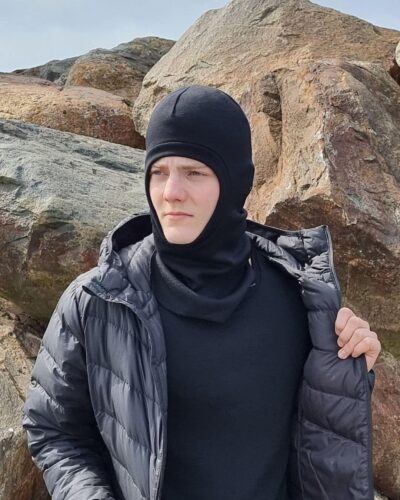 Lasten musta merinovillainen kypärämyssy nuoren miehen päässä kuvattuna.