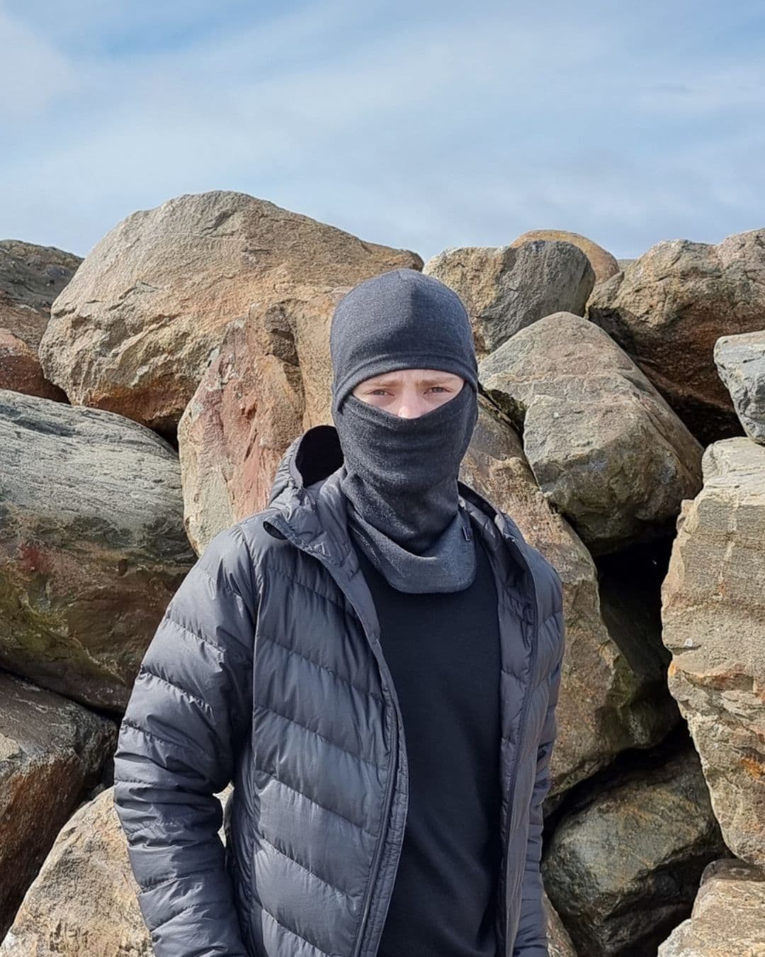 Lasten tummanharmaa merinovilla kypärämyssy (balaclava). Nuoren miehen päässä balaclava kasvojen yli vedettynä.