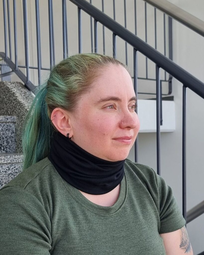 Naisten musta merinovillatuubihuivi vihreähiuksisen naisen kaulassa. Lähikuva sivulta.