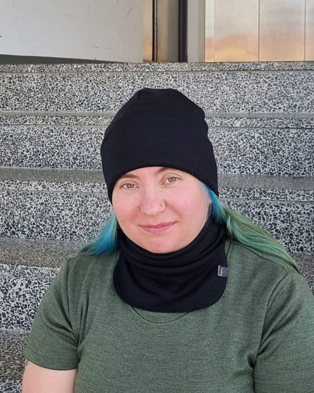Naisten musta merinovillapipo ja -tuubikauluri vihreähiuksisella naisella. Lähikuva edestä.