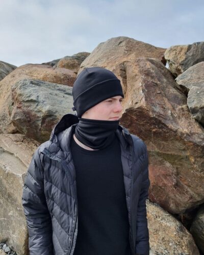 Lasten musta merinovillapipo ja tuubihuivi. Lasten musta merinovillapipo ja tuubihuivi nuoren miehen päällä sivusta kuvattuna.