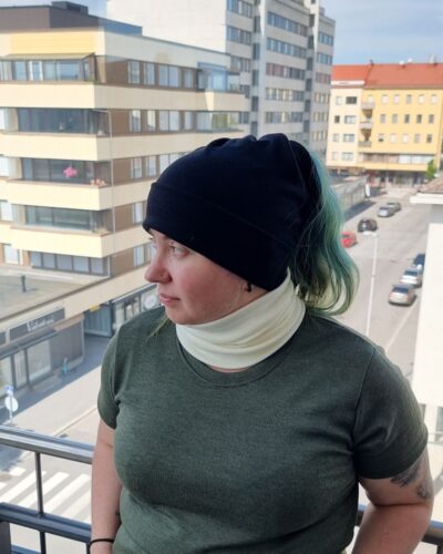 Naisten valkoinen merinovillatuubihuivi ja musta ponnaripipo, vihreähiuksisella naisella.