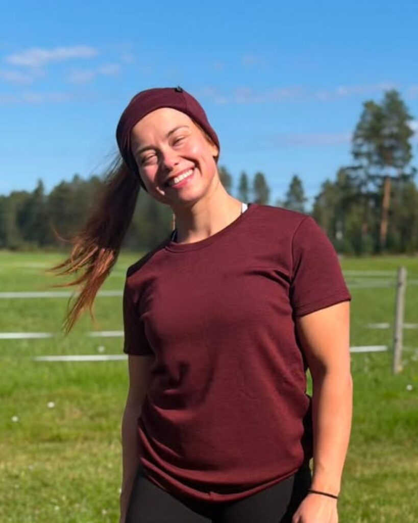 Naisten rubiiinpunainen merino t-paita naisen päällä maalaismaisemassa.