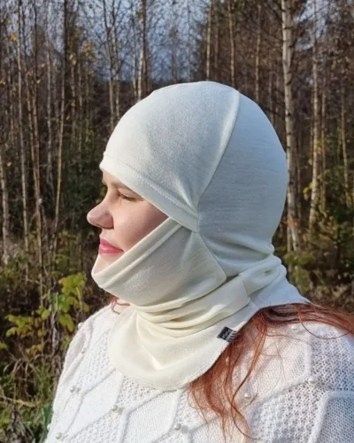 Aikuisten luonnonvalkoinen kypärämyssy kasvosuojalla (balaclava). Lähikuva sivusta, jossa naisella kypärämyssy päässään kasvot näkyvissä.