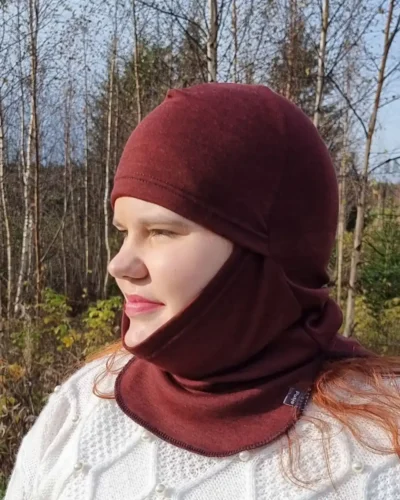 Aikuisten rubiininpunainen kypärämyssy kasvosuojalla (balaclava). Aikuisten rubiininpunainen kypärämyssy kasvosuojalla (balaclava). Lähikuva sivusta, jossa naisella kypärämyssy päässään niin, että kasvot on näkyvissä.