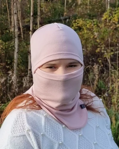 Aikuisten vaaleanpunainen kypärämyssy kasvosuojalla (balaclava). Lähikuva kypärämyssystä naisen päässä, kasvot suojattuna.
