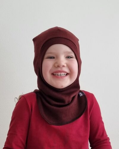 Lasten rubiininpunainen merinovillakypärämyssy. Lähikuva edestä kypärämyssy pienen tytön päässä.