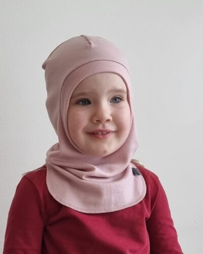 Lasten vaaleanpunainen merinovillakypärämyssy. Lähikuva edestäpäin pienestä tytöstä, jolla kypärämyssy päässään.