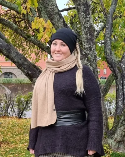Naisten kinuskinruskea merinovilla kaulahuivi ja musta ponnaripipo naisen päällä syksyisessä kaupunkimaisemassa.