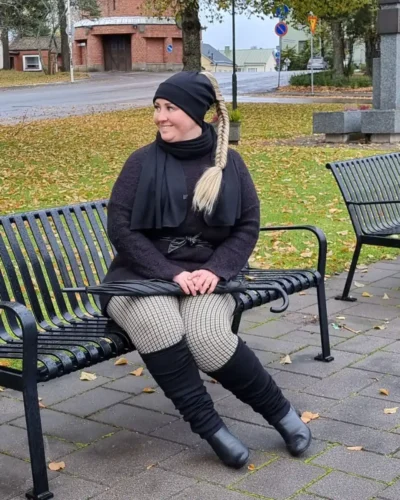 Pitkät mustat merinovilla säärystimet, kaulahuivi ja ponnaripipo. Pitkät mustat merinovilla säärystimet, kaulahuivi ja ponnaripipo syksyisessä maisemassa, puiston penkillä istuvan naisen päällä.