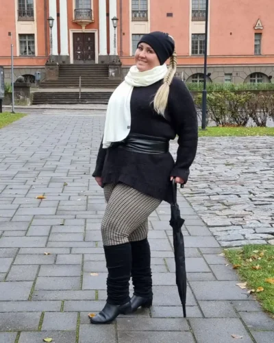 Pitkät mustat merinovilla säärystimet, luonnonvalkoinen kaulahuivi ja musta ponnaripipo. Pitkät mustat merinovilla säärystimet, luonnonvalkoinen kaulahuivi ja musta ponnaripipo, syksyiseen asuun pukeutuneen naisen päällä kaupungilla.