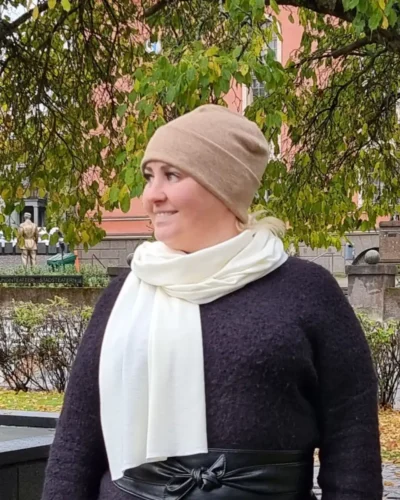 Naisten kinuskinruskea merinovillapipo ja luonnonvalkoinen kaulahuivi naisen päällä syksyisessä kaupunkimaisemassa.